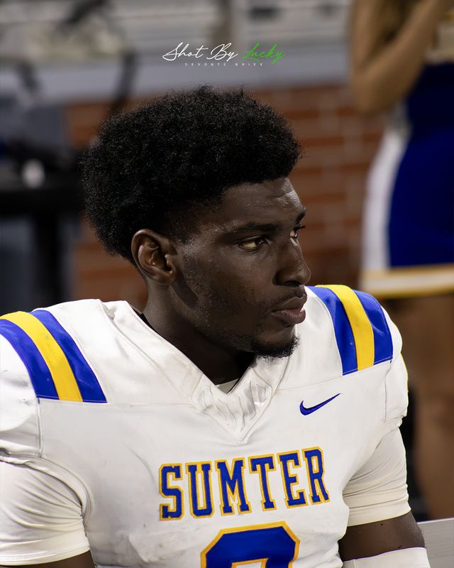 A player on the sideline, helmet off, watching the game